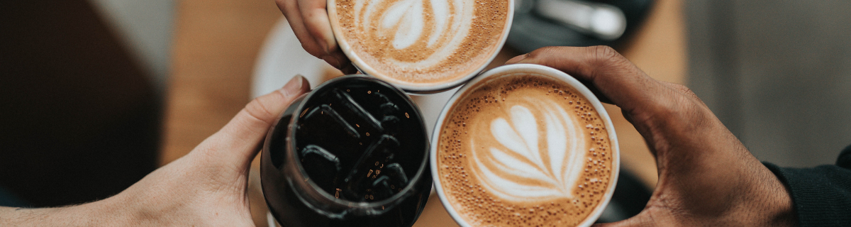 Birds eye view of three white hands holding cups of coffee into frame. 