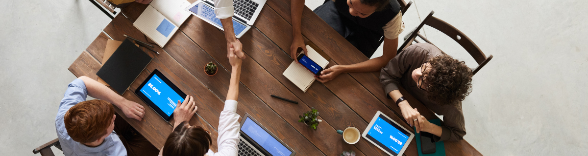 Birds eye view of group of men and women with laptops sat around a wooden table 